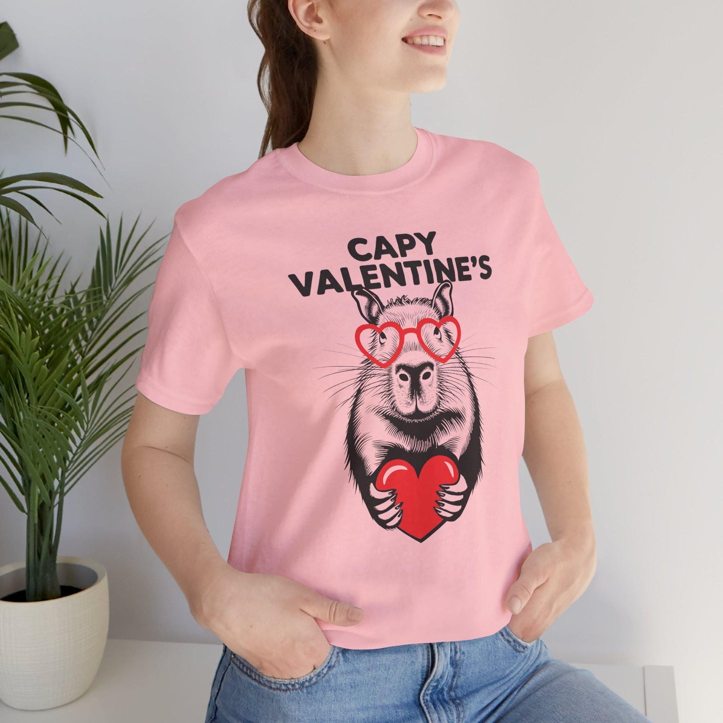 a woman wearing pink a t - shirt with an image of a capybara holding a heart that says Capy Valentines, Capybara Valentines Shirt, Gift For Her, Capybara Lover Gift, Funny Capybaras Shirt, Valentines Day Gifts, Animal Lover Gifts, Capybaras tee