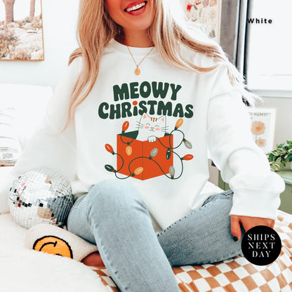 a woman sitting on a bed wearing a merry christmas sweatshirt, Meowy Christmas Sweater - Catmas Sweatshirt, Meowy Christmas Sweatshirt, Gift For Cat Mom, Cute Cat Mom Sweatshirts, Holiday Sweatshirts